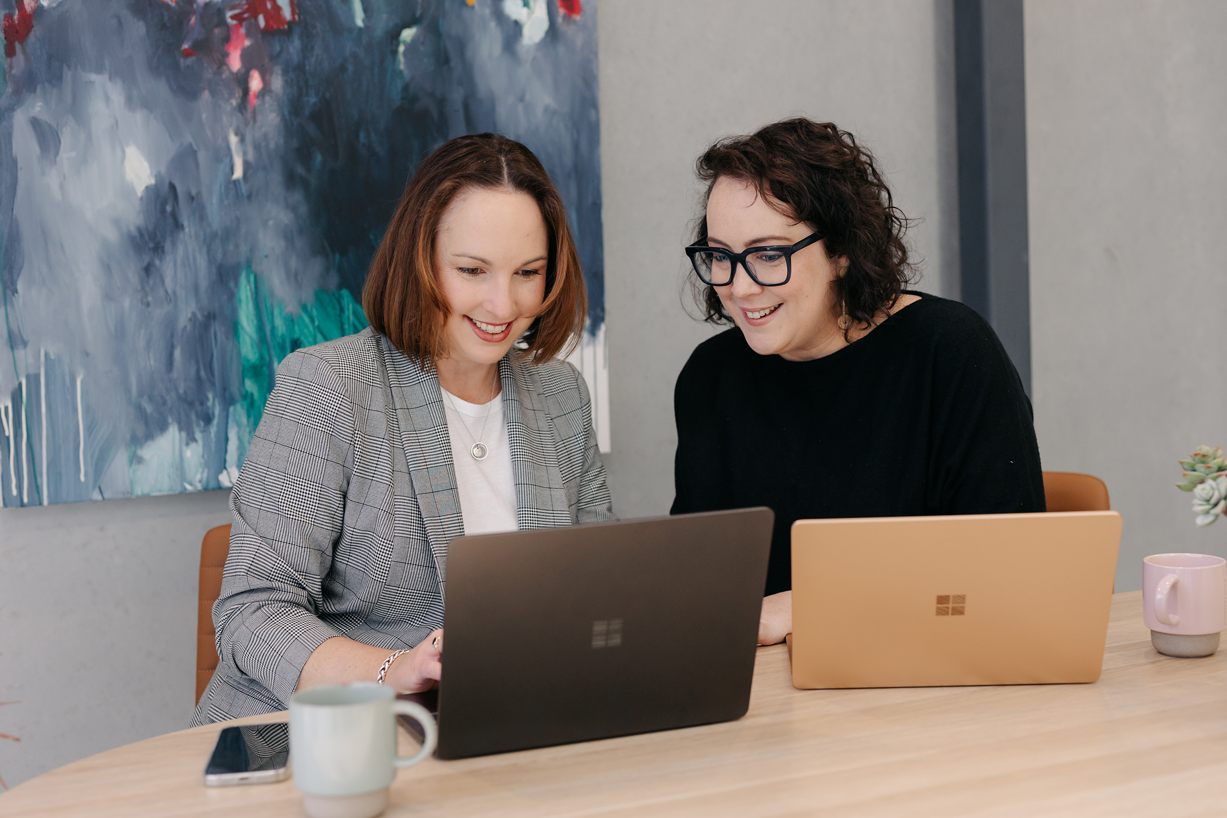 Stacey Kelly and Julia Fiore smiling together at a laptop in the Seed People Consulting office.