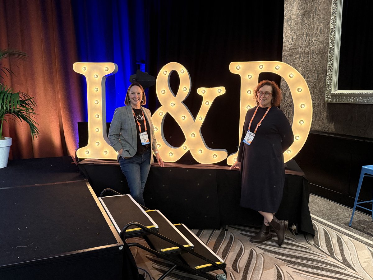 Stacey Kelly and Julia Fiore of Seed People Consulting at the 2026 HR and L&D Innovation and Tech Fest in Auckland, standing beside a large light-up 'L&D' marquee sign.